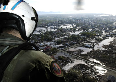 A U.S. Navy man looks down from a helicopter at the flooded land below
